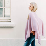 female wearing light pink wrap over her shoulders walking outside in front of a white building