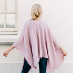 female wearing light pink wrap over her shoulders turned around outside in front of a white building
