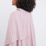 close up of female wearing light pink wrap over her shoulders turned around on a white background
