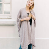 female wearing beige wrap over her shoulders standing outside in front of a white building