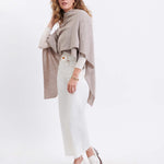 female wearing beige wrap over her shoulders standing sideways in front of a white background