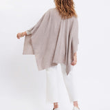 female wearing beige wrap over her shoulders standing backwards in front of a white background