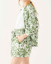 side detail of female wearing white floral linen shirt with matching short set on white background