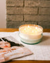 large clear glass orangerie candle bowl lit sitting on a table near a magazine 