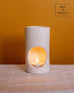 white ceramic scented lit oil burner sitting on a blanket on an orange background