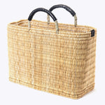 large straw basket wrapped with black leather handle on a white background at an angle