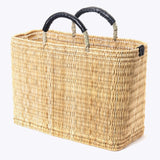 large straw basket wrapped with black leather handle on a white background at an angle