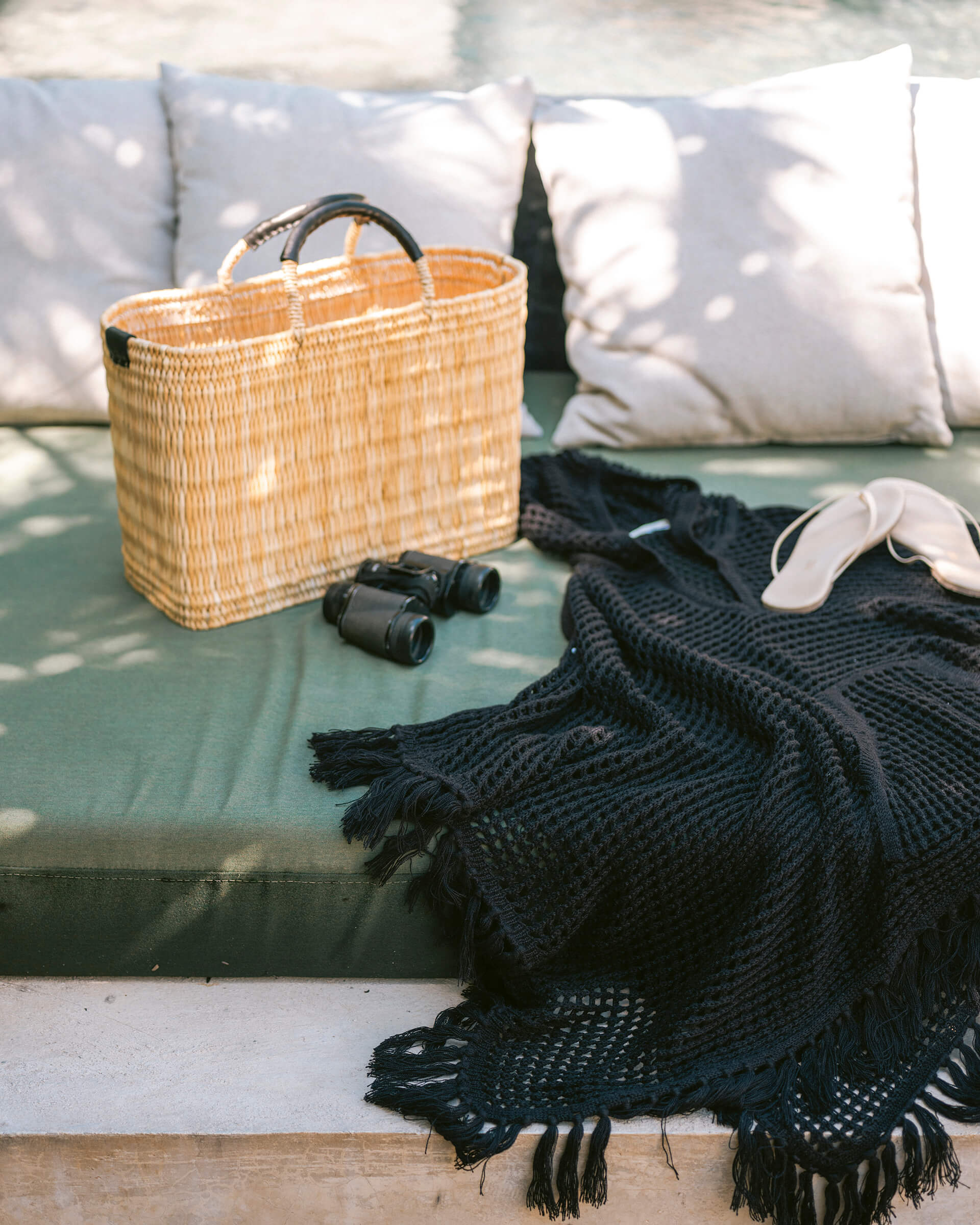 medium straw basket wrapped with black leather handle sitting on a day bed outside 