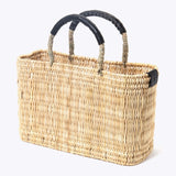 small straw basket wrapped with black leather handle on a white background at an angle