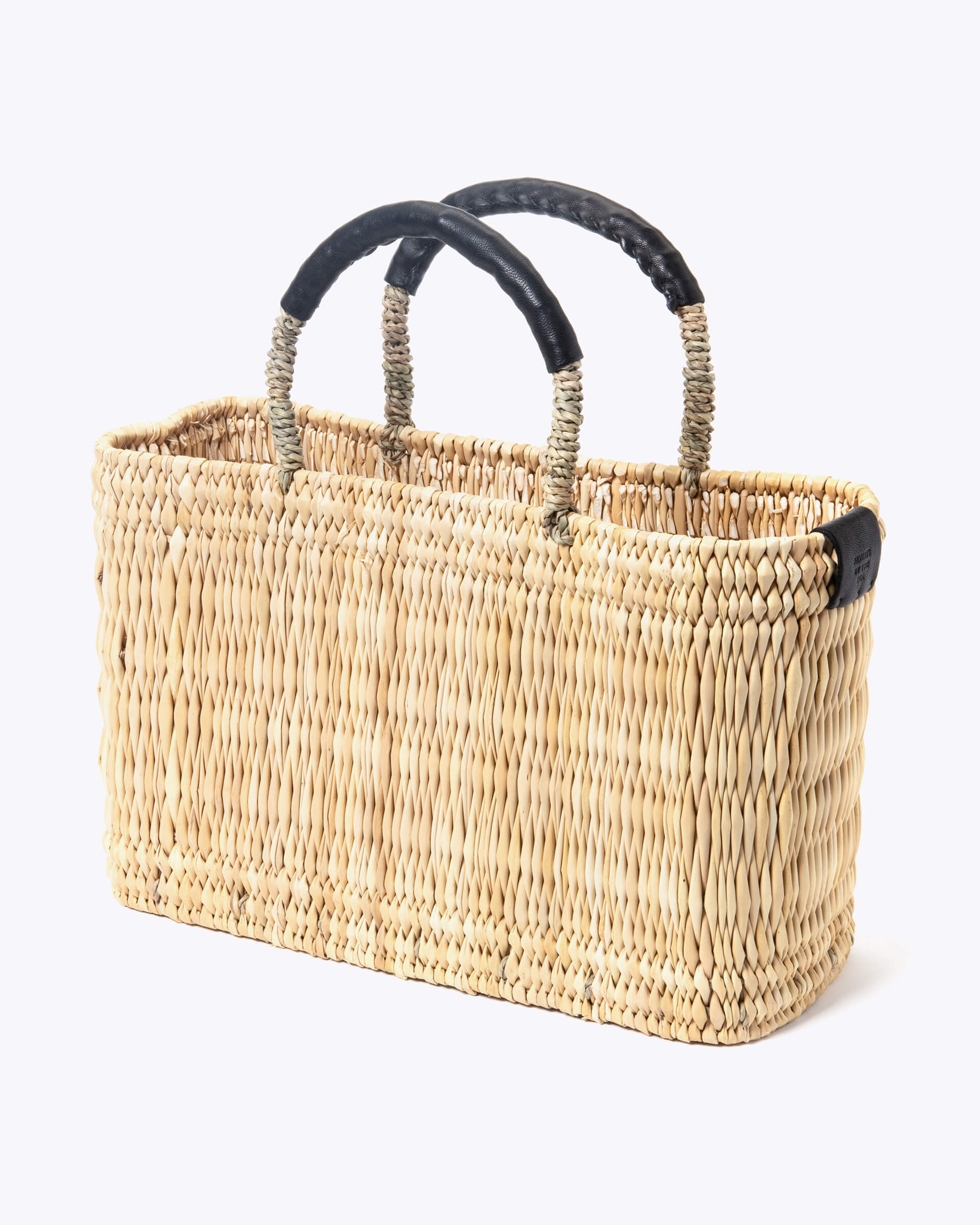 small straw basket wrapped with black leather handle on a white background at an angle
