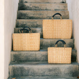 small, medium, large straw basket wrapped with black leather handles sitting on different stairs 