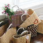 six different colored and sized straw baskets stacked near a window on a hardwood floor