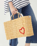 female holding medium red heart straw basket wrapped w/ neutral leather handle on white background