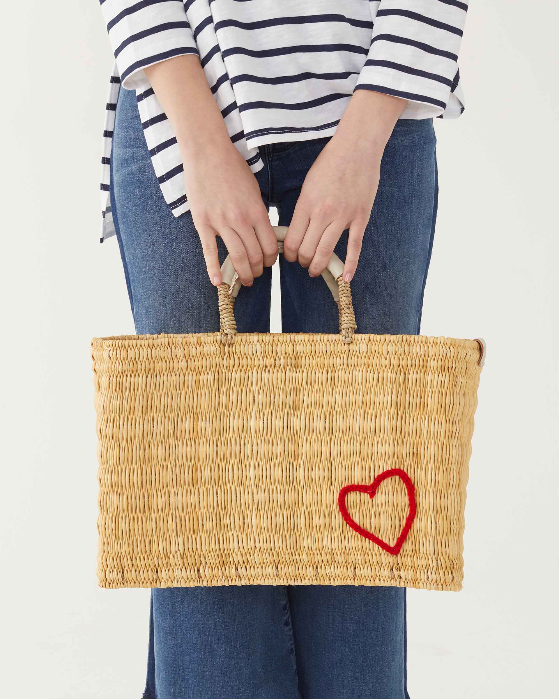 female holding medium red heart straw basket wrapped w/ neutral leather handle on white background