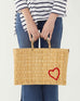 female holding medium red heart straw basket wrapped w/ neutral leather handle on white background