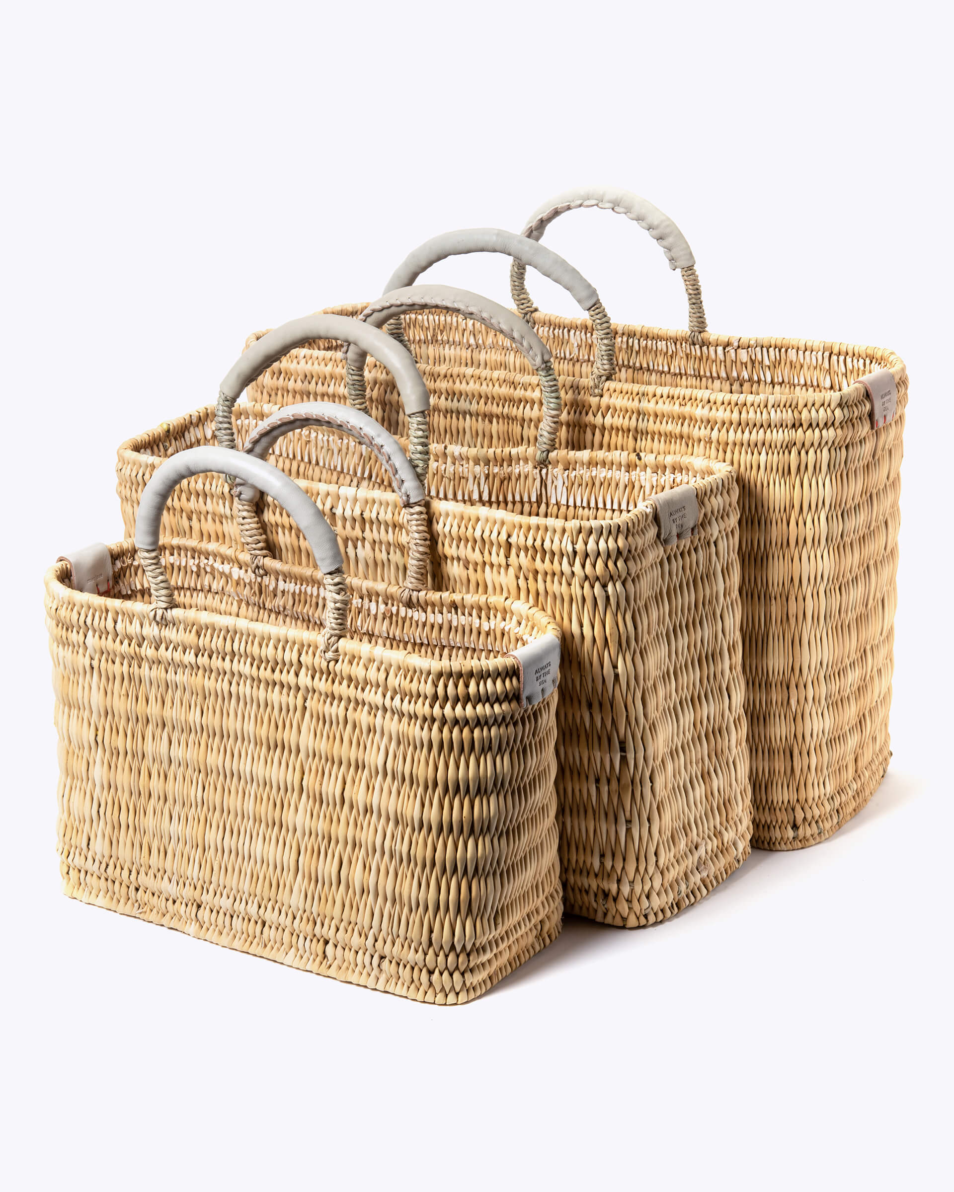 small, medium, large straw basket wrapped with neutral leather handles on white background