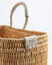 close up of medium straw basket with leather imprint of always by the sea on a white background 