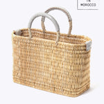 small straw basket wrapped with neutral colored leather handled on a white background at an angle