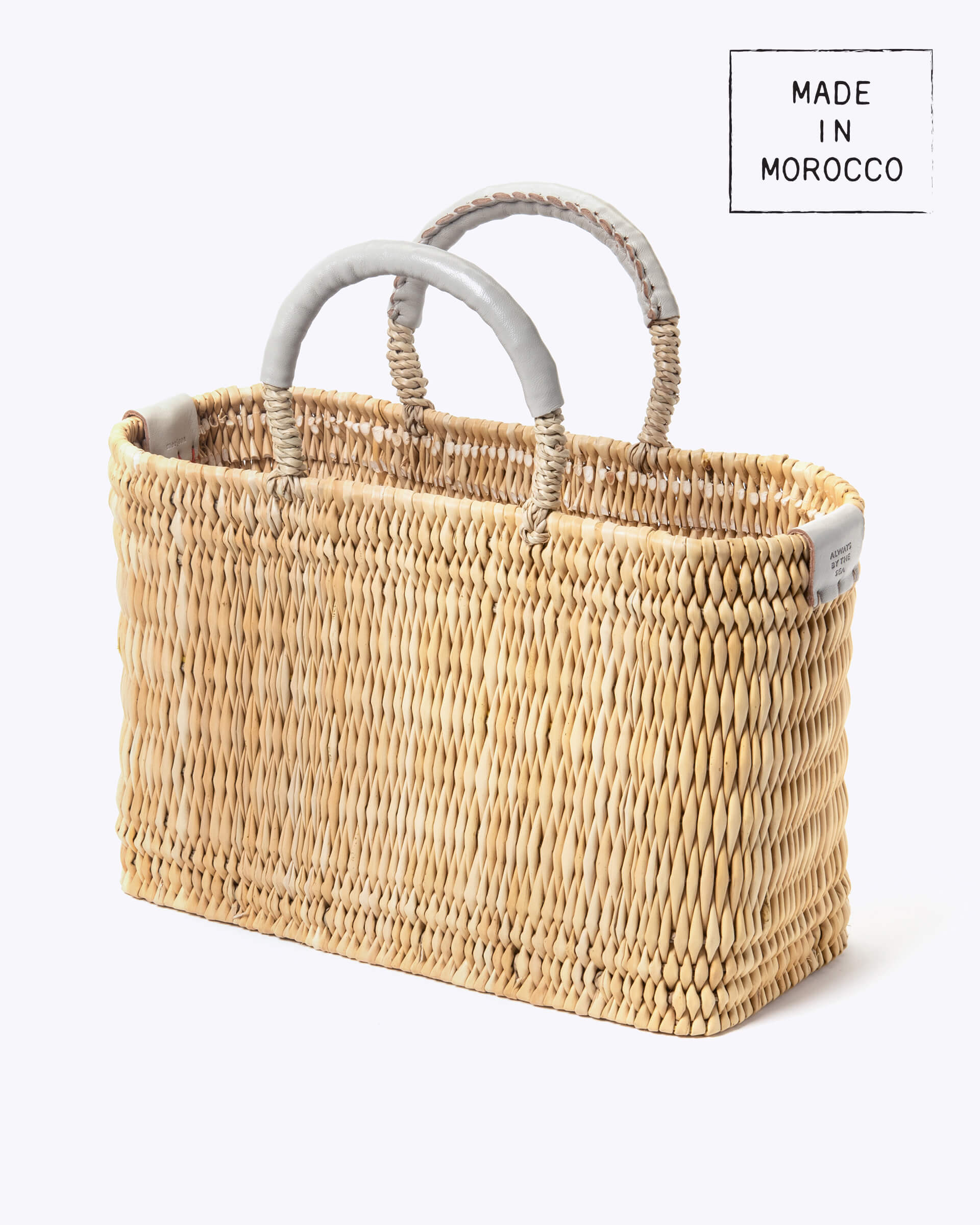 small straw basket wrapped with neutral colored leather handled on a white background at an angle
