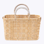 small straw basket wrapped with neutral colored leather handles on a white background