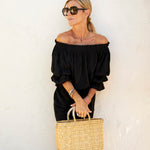 blonde female holding small straw basket with a neutral colored handle leaning against white wall