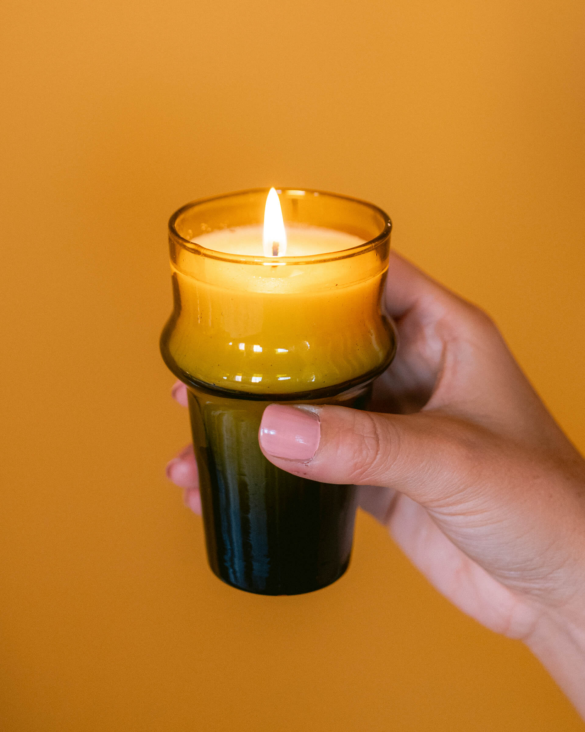 female holding a tall dune umber glass candle on an orange background