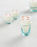 tall clear glass orangerie candle sitting with short clear glasses on a white background 