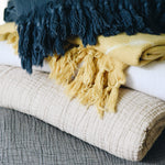 grey, light beige, yellow, white, and dark blue gauze and shibori blankets stacked on eachother