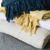grey, light beige, yellow, white, and dark blue gauze and shibori blankets stacked on eachother