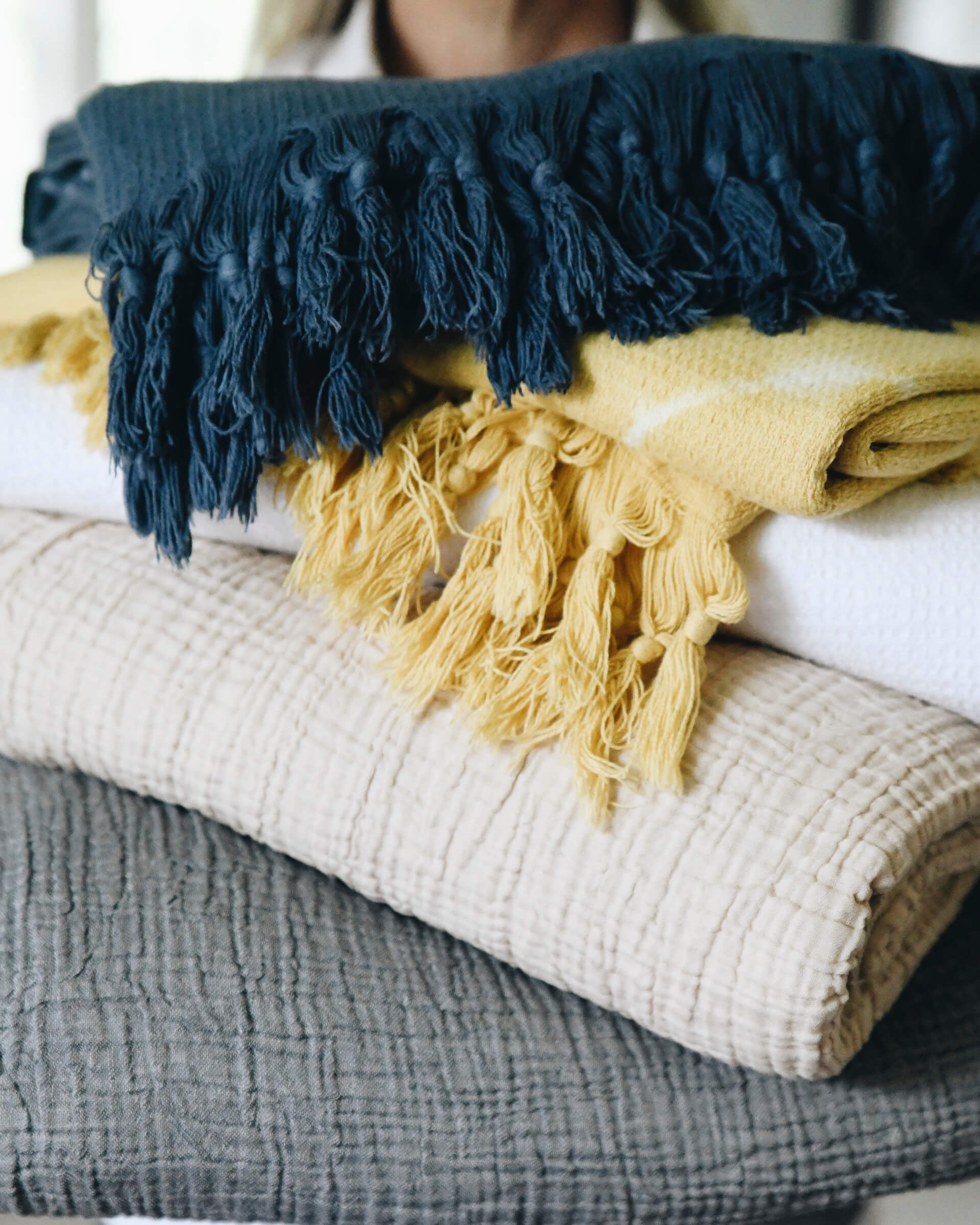 grey, light beige, yellow, white, and dark blue gauze and shibori blankets stacked on eachother