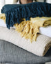 grey, light beige, yellow, white, and dark blue gauze blanket stacked on top of eachother