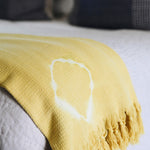 yellow shibori blanket with white fringe detailing laying folded on a couch