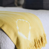 yellow shibori blanket with white fringe detailing laying folded on a couch