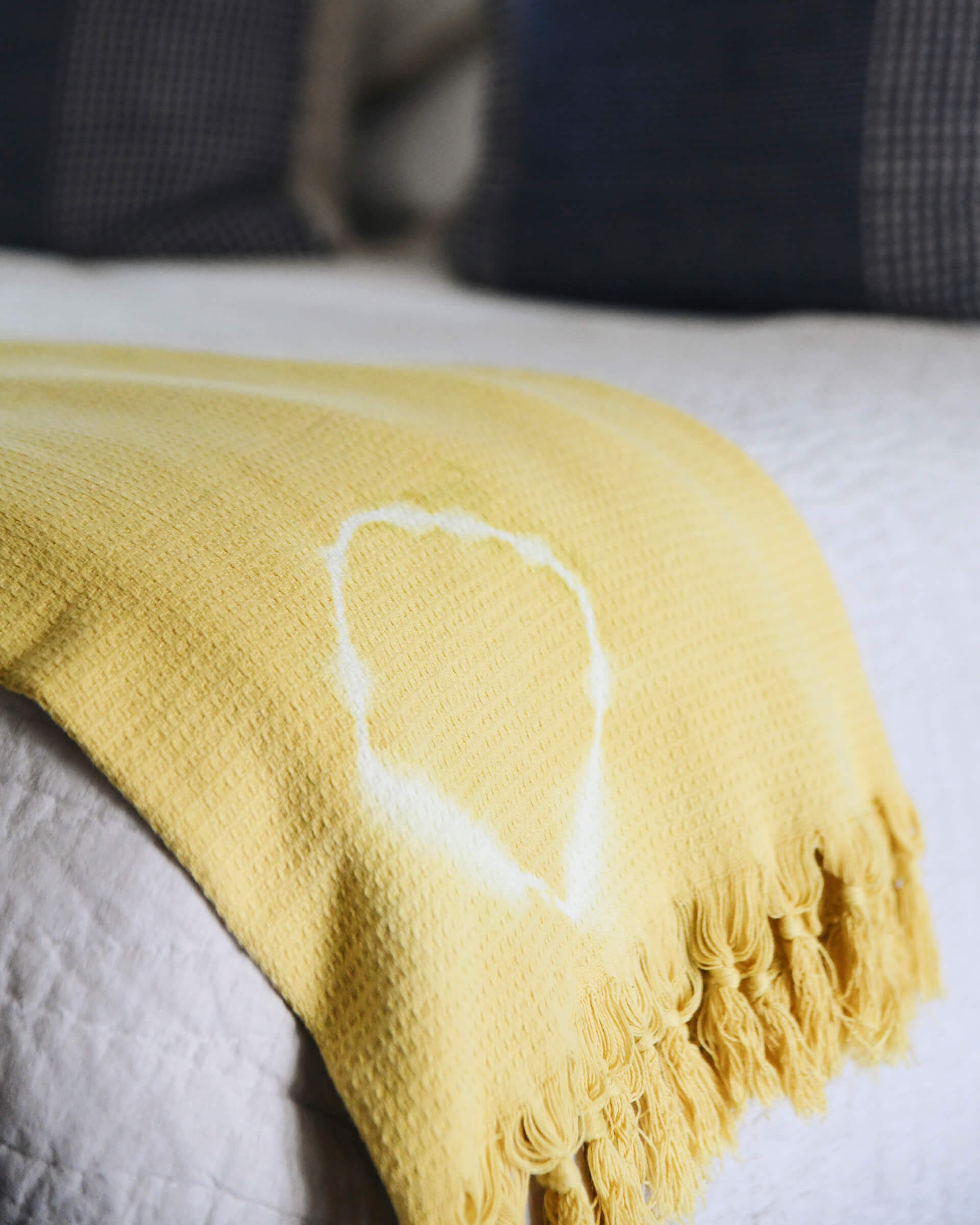 yellow shibori blanket with white fringe detailing laying folded on a couch