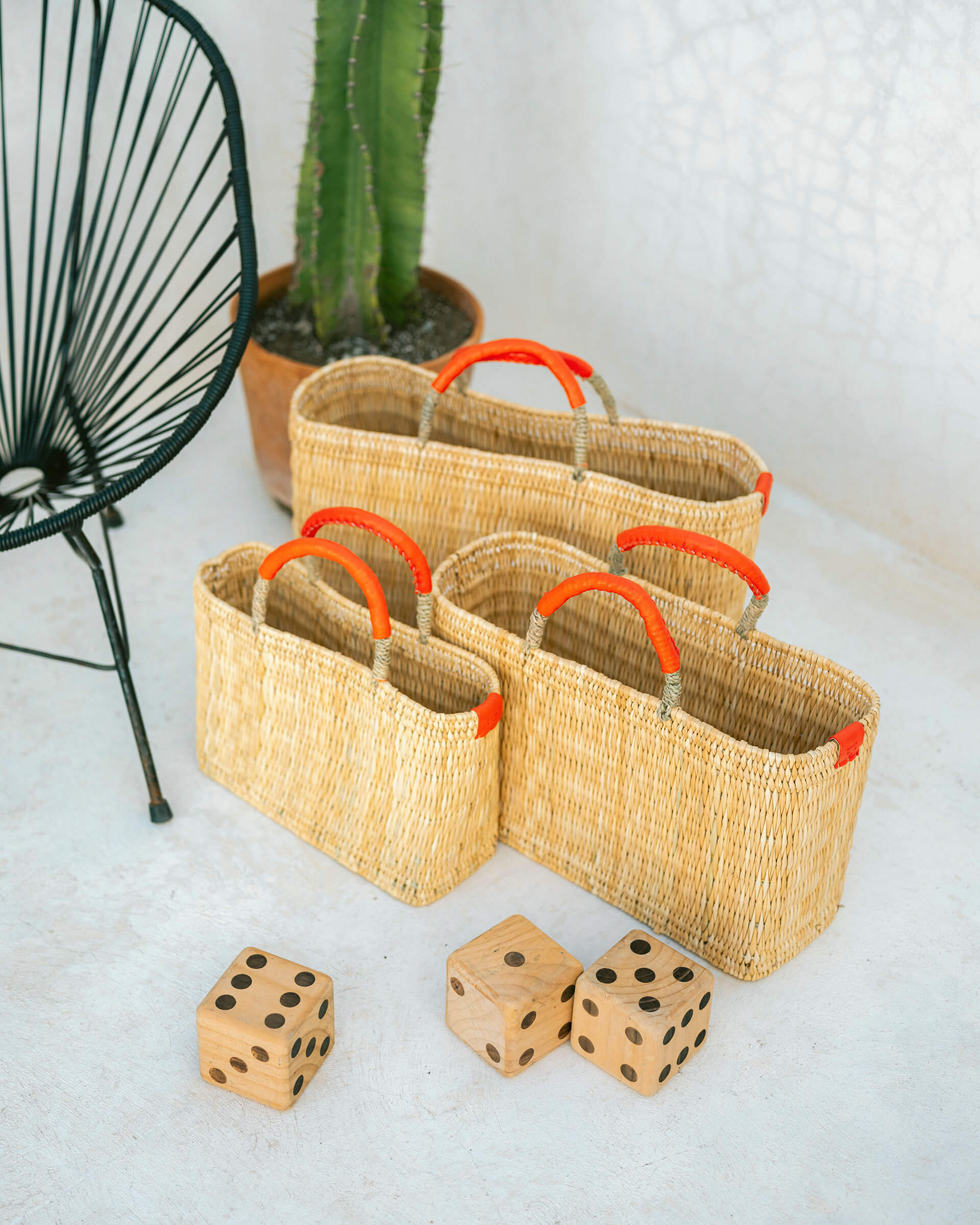 small, medium, large straw basket wrapped with orange leather handles clustered near dice and chair