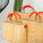 small, medium, large straw basket wrapped with orange leather handles clustered near a cactus