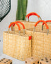 small, medium, large straw basket wrapped with orange leather handles clustered near a cactus