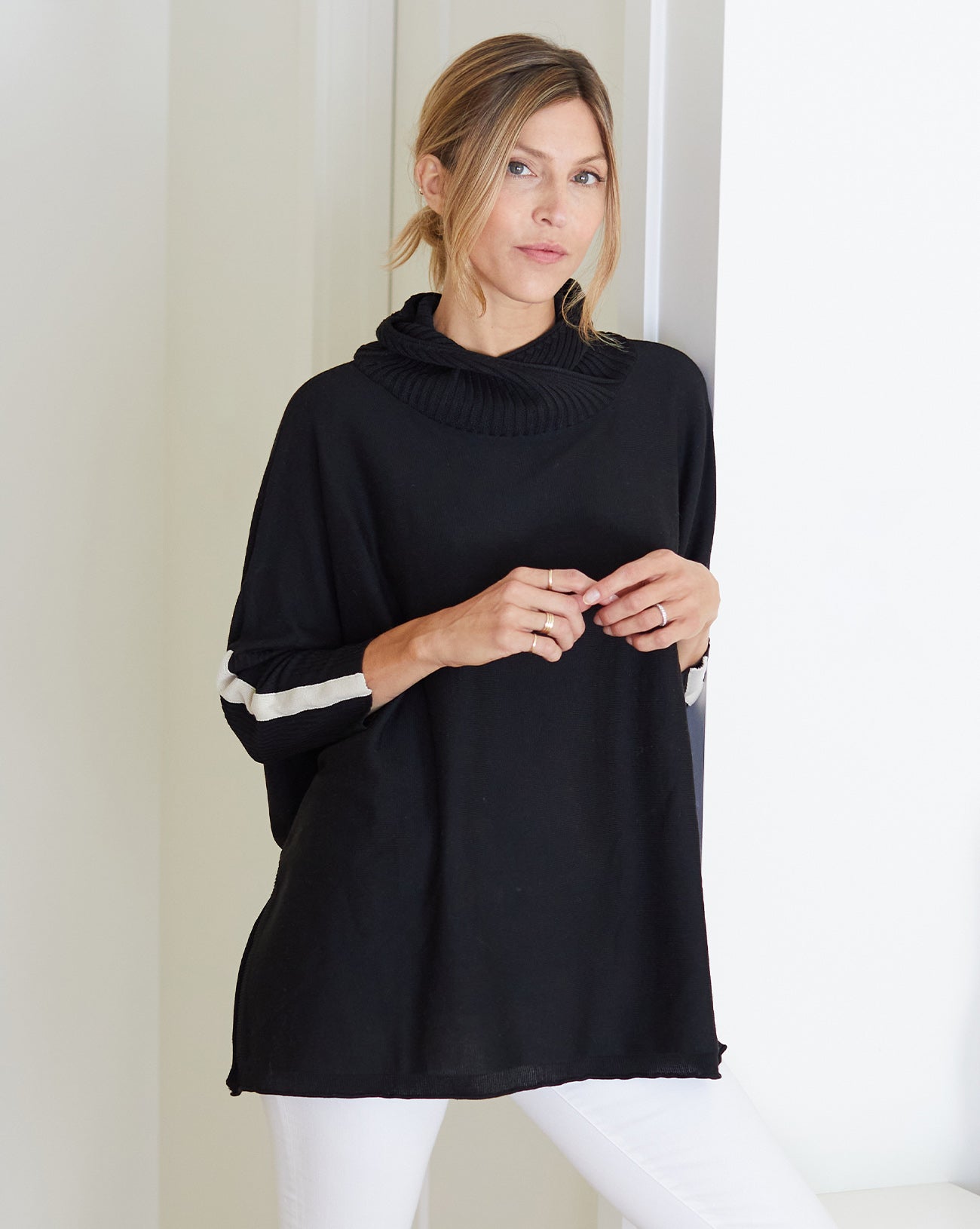woman wearing mersea newport sweater in black with white accent stripe down lower sleeve with a split front turtleneck and ribbed sleeves