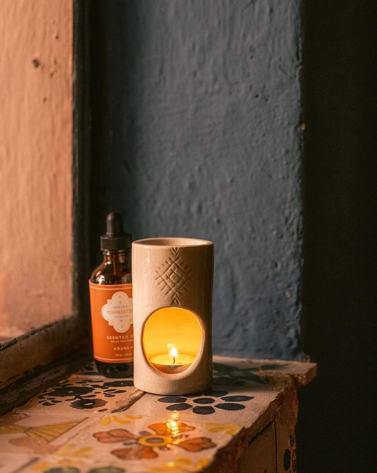bottle of dune scented oil burner next to white ceramic candle holder on window ledge 