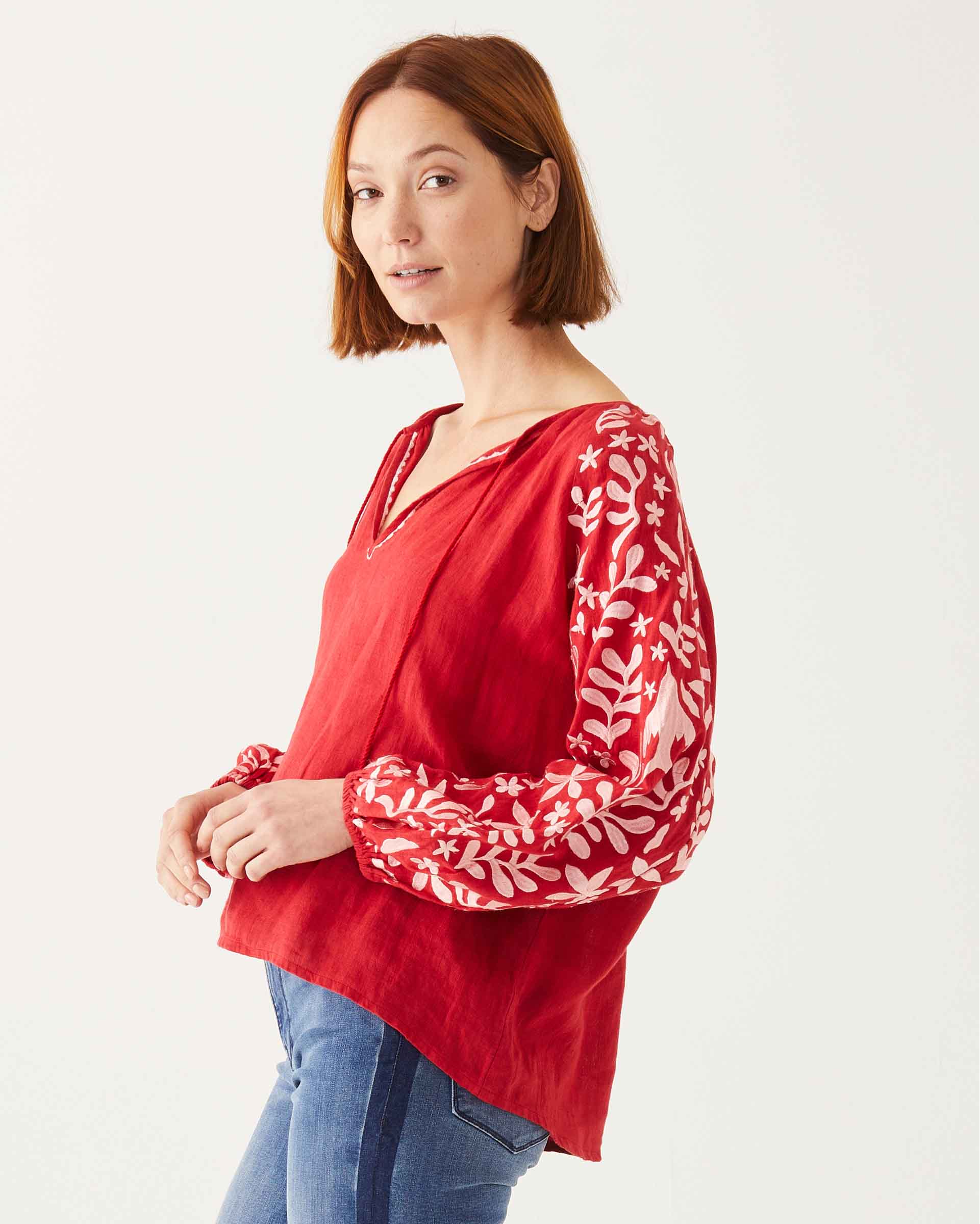 female wearing red and white embroidered blouse with tassel ties sideways on a white background