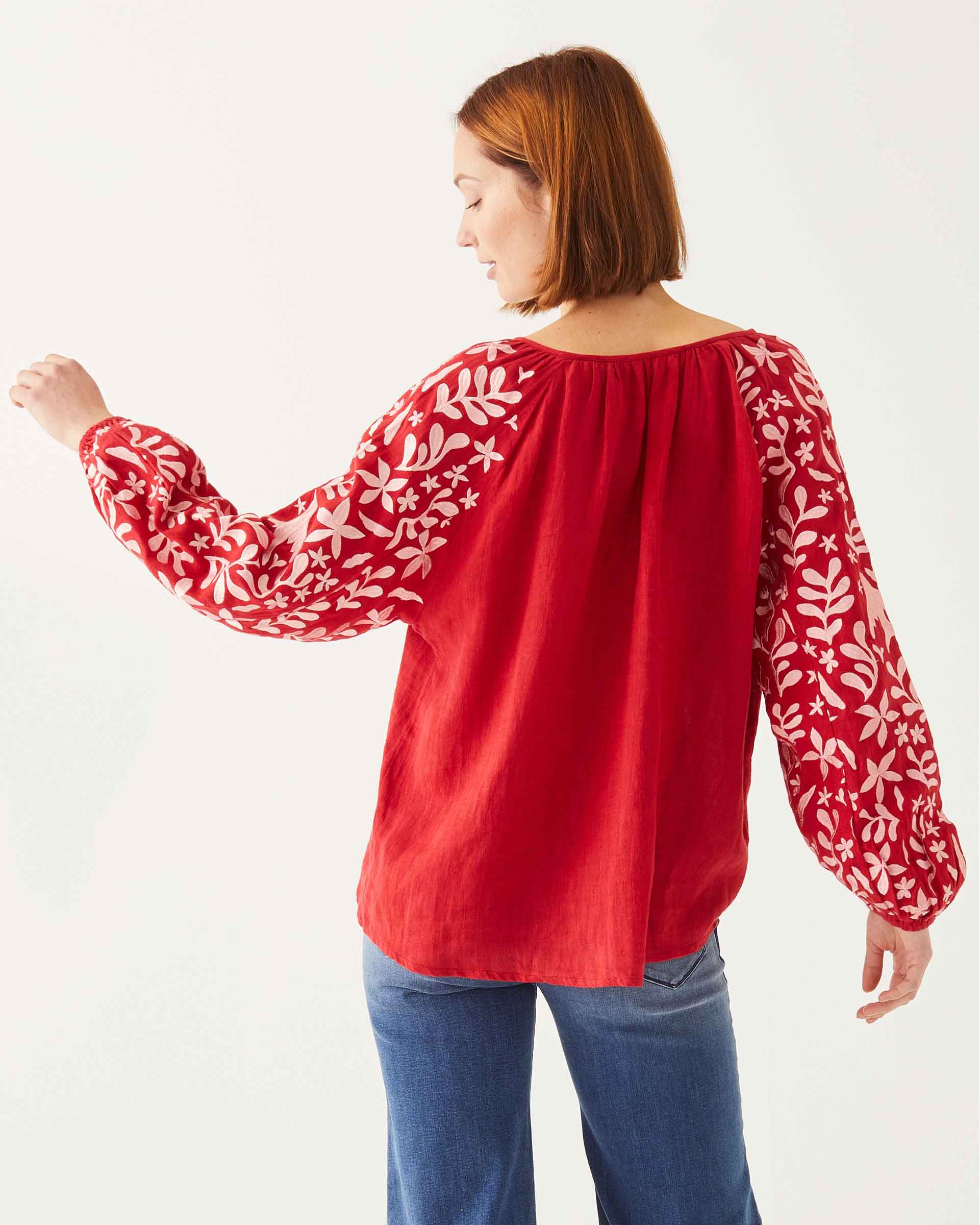 female wearing red and white embroidered blouse with vines and birds backwards on white background