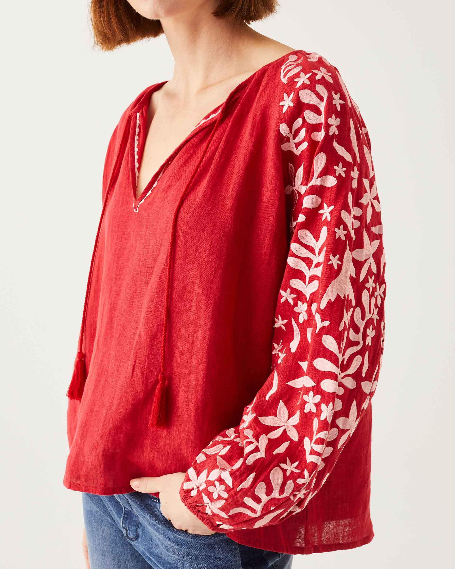 front detail of female wearing red & white embroidered blouse with tassel ties on white background