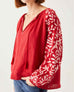 front detail of female wearing red & white embroidered blouse with tassel ties on white background
