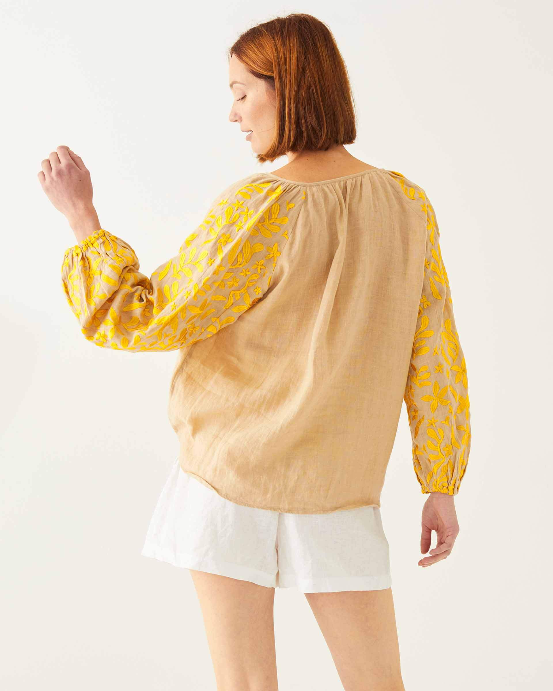 female wearing tan and yellow embroidered blouse with vines and birds backwards on white background