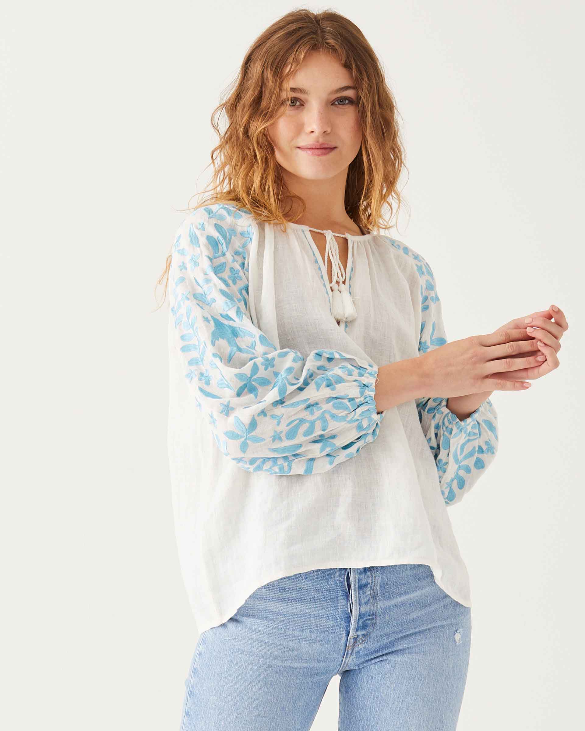 female wearing white and blue embroidered blouse with v-neckline on a white background