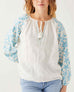 front detail of female wearing white & blue embroidered blouse with tassel ties on white background