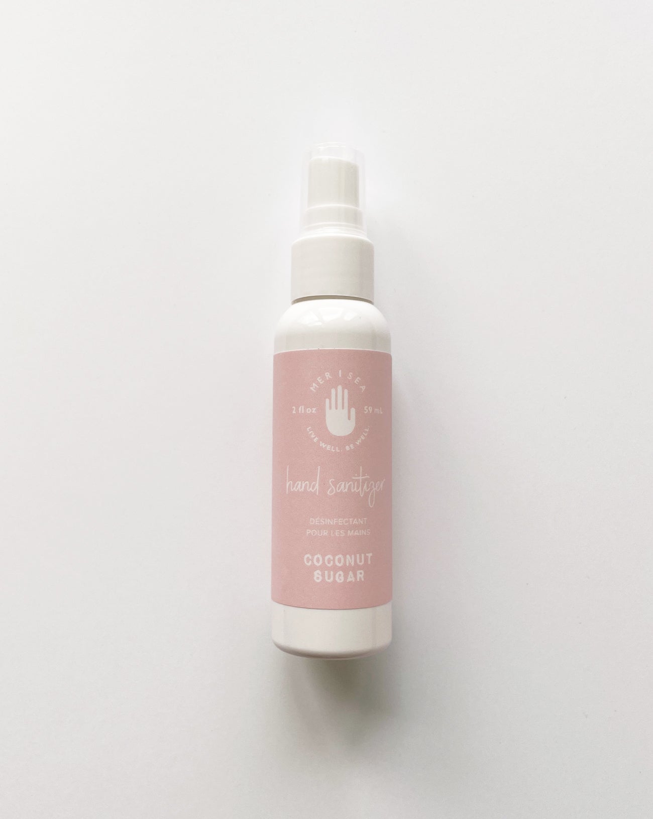 coconut sugar hand sanitizer in a white bottle with a pink label laying on a white background