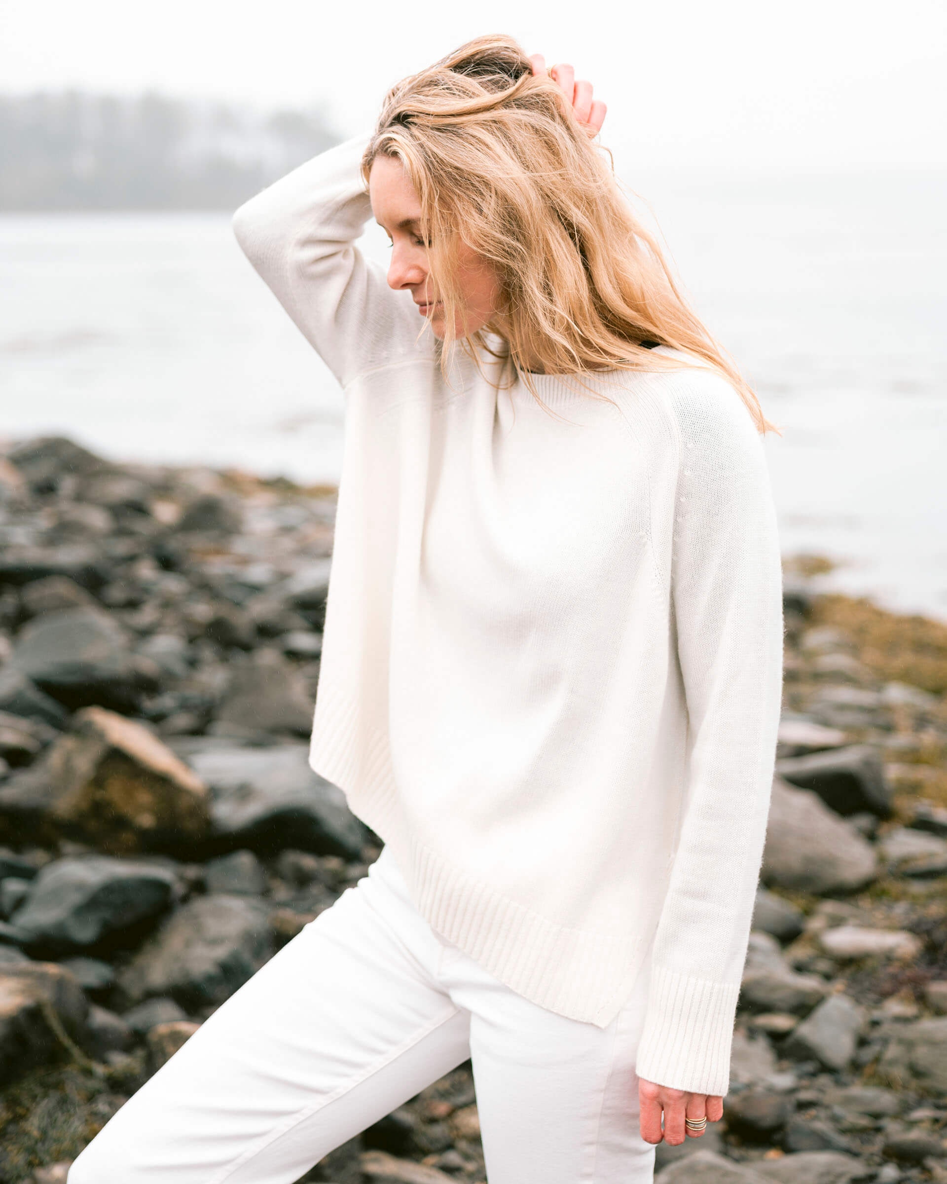 woman wearing mersea banff sweater in winter white standing  on rocks