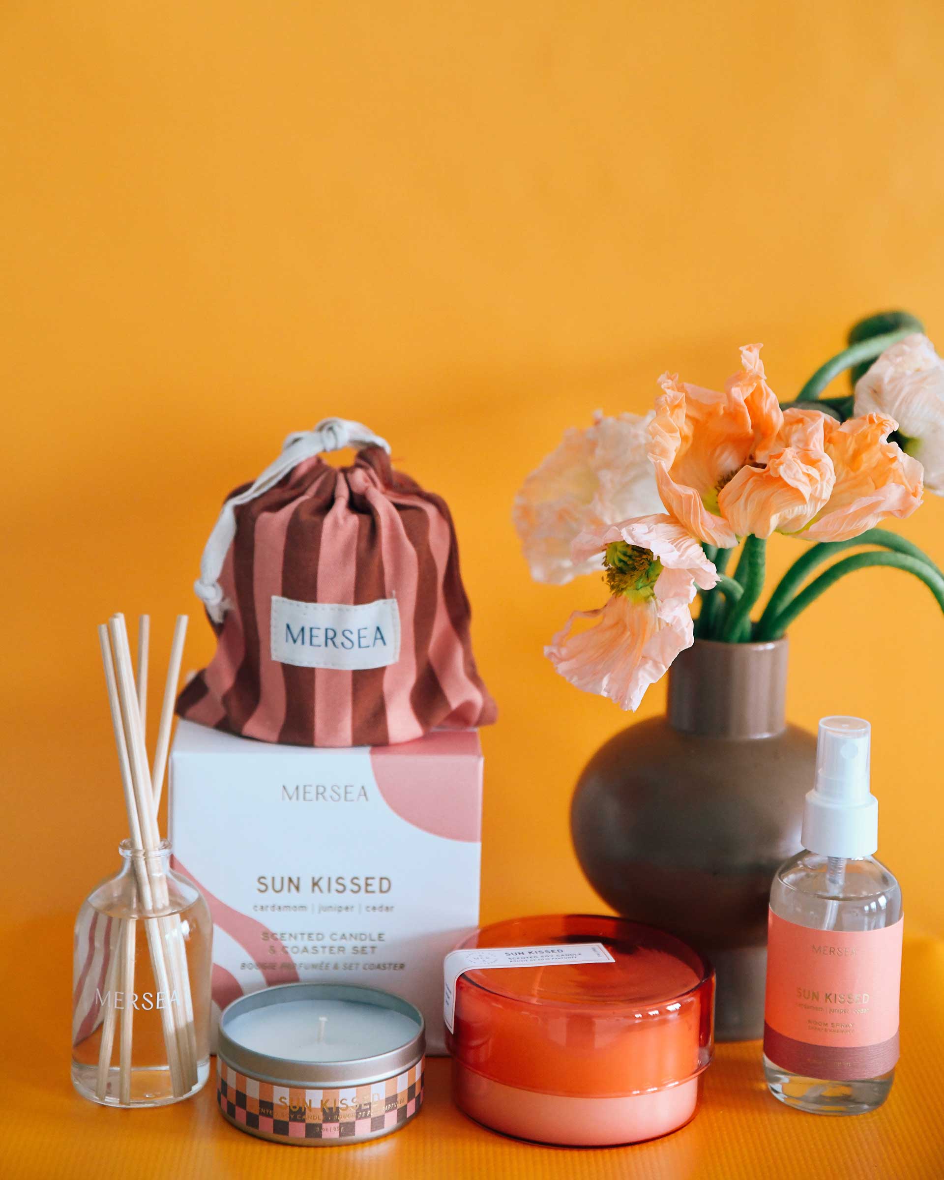 Sunkissed diffuser, candles, room sprays and a flower on an orange background