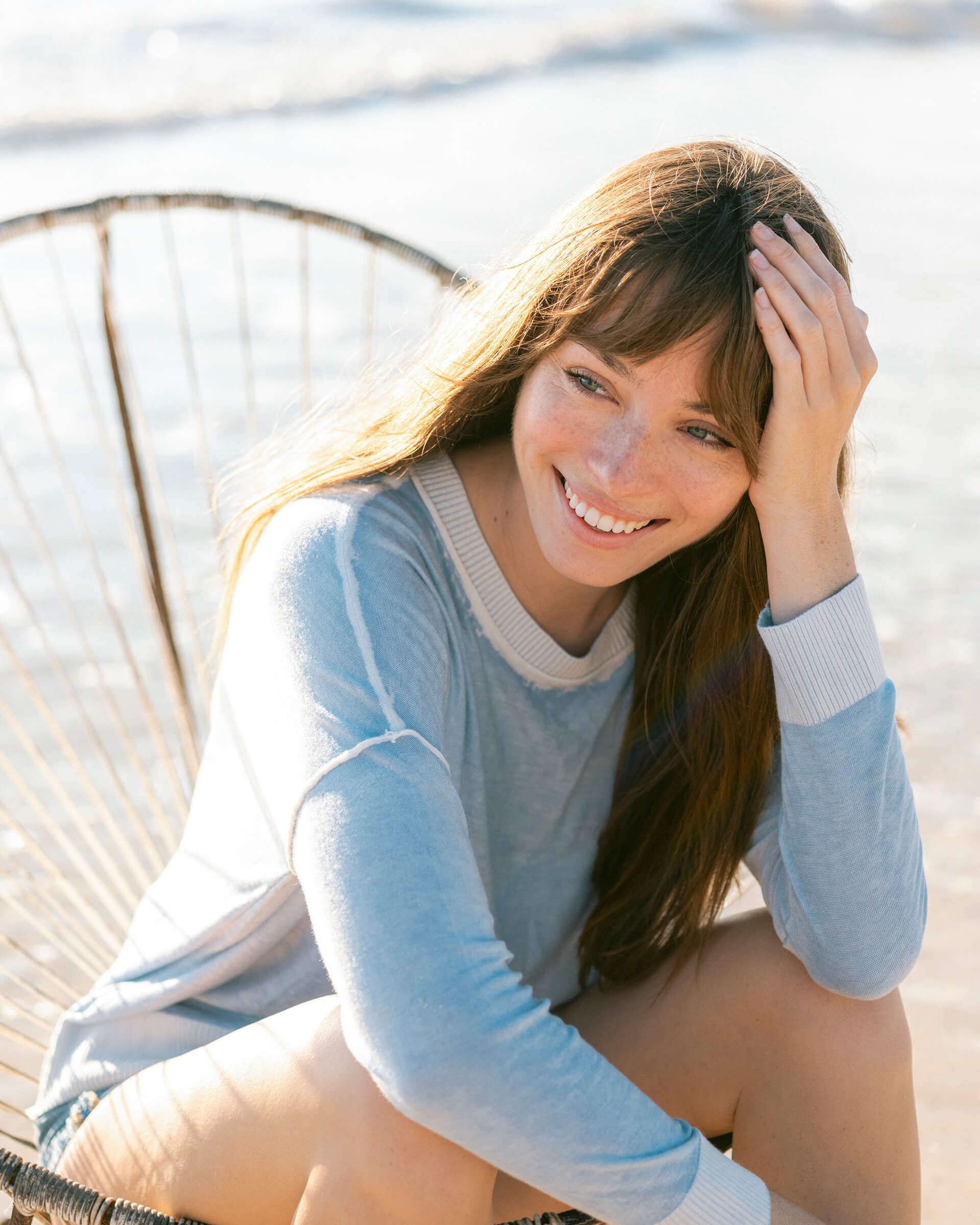brunette female wearing light blue sweater sitting on a chair on the beach 